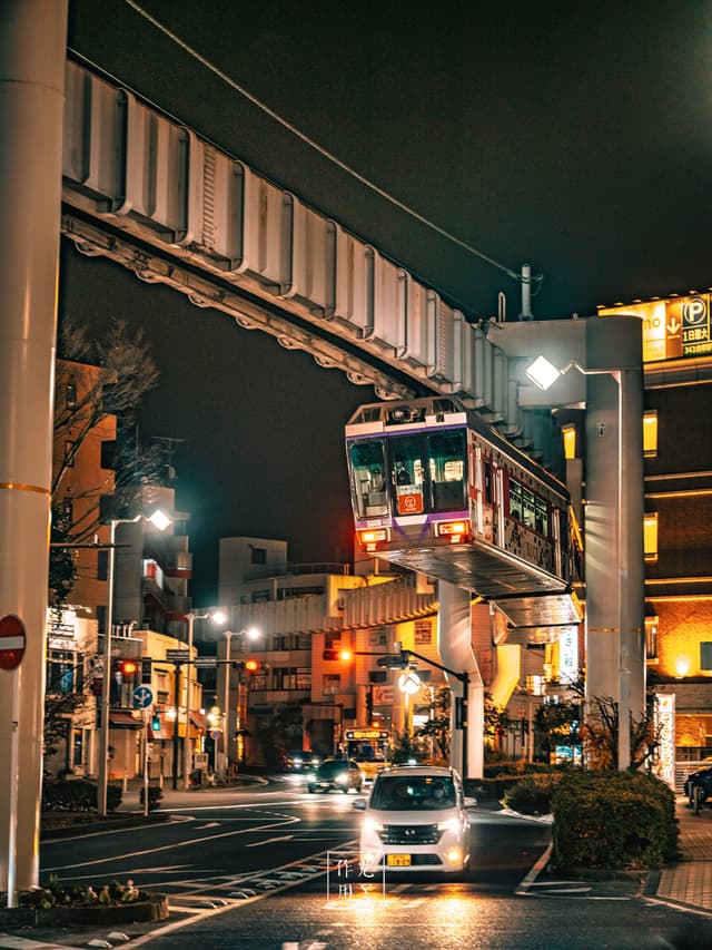 suspended tram, elevated track, car, streetlamp, illuminated storefronts