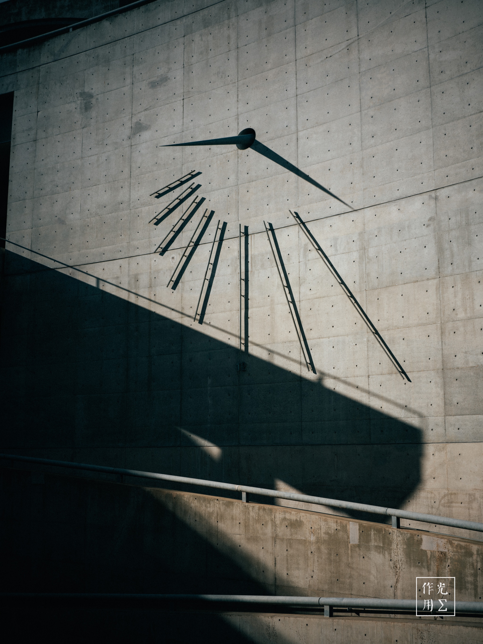 Slender steel rods fan out like fallen spokes against a monolithic concrete plane, their sharp silhouettes fractured by the lowering sun. Two stark clock hands hover above the chaos, casting elongated shadows that slice the wall in a midnight-blue diagonal. Rough, pale-gray textures absorb the light, while the pronounced shadow of a stairway railing carves a bold, geometric counterpoint. An atmosphere of suspended time and quiet tension hangs in the air, as if the moment just before midnight has been fragmented—and paused—on this raw, urban canvas